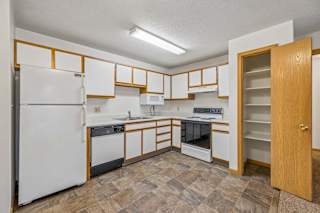 Spacious apartment kitchen with white cabinets, white appliances, a freestanding oven, durable flooring, and a built-in pantry for additional storage.