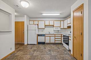 Open apartment kitchen with white cabinets, white appliances, durable flooring, and a pass-through breakfast bar connecting to the adjacent living area.