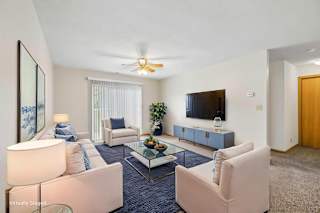 Virtually staged living room with two armchairs, a wall-mounted TV, coffee table, sliding glass door, and neutral finishes.