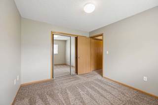 Bright apartment bedroom with carpeted flooring, neutral walls, mirrored sliding closet doors, and a separate walk-in closet for additional storage.