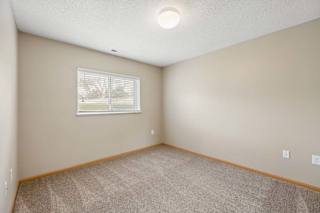 Bright apartment bedroom with carpeted flooring, neutral walls, and a window with blinds providing natural light.