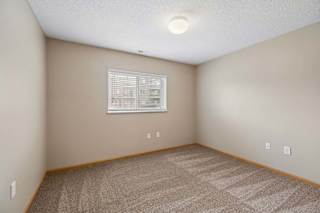 Bright apartment bedroom with carpeted flooring, neutral walls, and a window with blinds providing natural light.