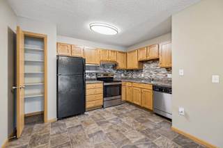 Apartment kitchen with wood cabinetry, a tile backsplash, laminate countertops, black and stainless steel appliances, and a pantry with built-in shelving in a functional U-shaped layout.