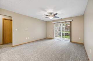Living room with a ceiling fan and sliding glass door opening to a ground-level patio and landscaped green space.