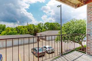 a covered balcony with a metal railing, overlooking detached garages and green trees
