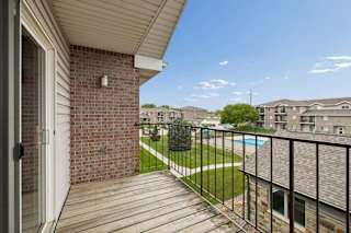 A balcony with a black railing and a brick wall with a pool view.