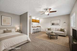 Virtually staged studio apartment featuring a sleeping area, living space, coffee table, ceiling fan, and partial view of the kitchen.