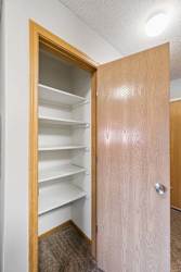 Apartment pantry or storage closet with built-in shelving, a wood-finish door, and convenient storage space located off the main living area.