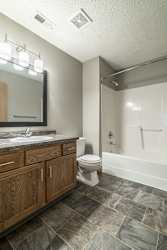 a bathroom with wooden cabinets, a granite vanity sink, a mirror, and a combination shower and tub