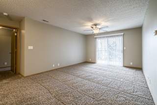 a carpeted living room with a ceiling fan and a sliding glass door to a balcony