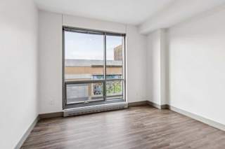 A bedroom with hardwood-style flooring, and a floor-to-ceiling window.