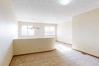 A carpeted loft bedroom with a view open to below, two bright windows, and a ceiling fan.