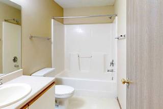 A bathroom with a white and oak vanity sink, tall mirror, towel rack, and combination shower and tub.
