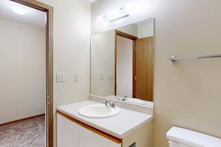 A bathroom with a white and oak vanity sink, tall mirror, towel rack.