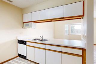 A galley kitchen with white cabinets with oak trim, white appliances, a double-basin sink, and a pass-through window countertop.