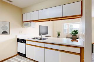 A kitchen with a white counter, white cabinets, and a pass through to the living room.