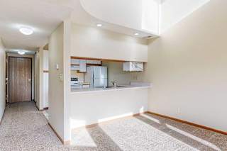A carpeted living room with access to the kitchen via a pass-through window countertop, and a hallway connecting to the front entryway.