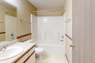 A bathroom with a vanity sink, large mirror, towel rack, and tub shower.