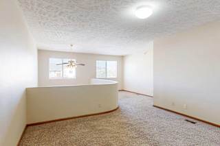 A loft bedroom with two windows, a ceiling fan, and a opening to the living room below.