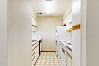 A galley kitchen featuring white cabinets with oak trim, white appliances, and a passthrough countertop to living room.