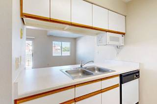 A kitchen with white cabinets with oak trim, a double basin sink, and a passthrough counter to the living room.