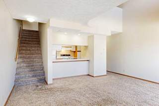 A carpeted living room with access to the kitchen via a pass-through window countertop, and a staircase to the upper loft area.