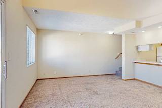 A carpeted living room with a window, access to the kitchen via a pass-through window countertop, and a staircase to the upper loft area.