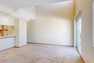 A carpeted living room with access to the kitchen via a pass-through window countertop, and a staircase to the upper loft area.