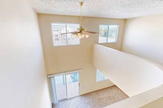 An opening in the loft to the living room below, with a view of three windows and a sliding glass door.