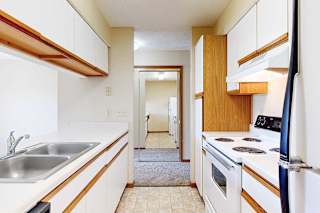A galley kitchen featuring white cabinets with oak trim, white appliances, and a passthrough countertop window.
