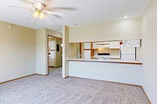 A living area with a ceiling fan and a view of the kitchen with white and oak cabinets.