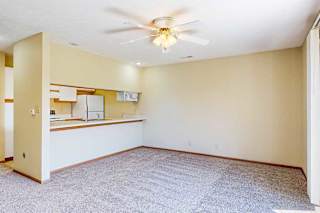 A living area with a ceiling fan and a view of the kitchen.