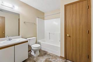 Apartment bathroom with a single-sink vanity, large mirror, toilet, tub/shower combination, and durable flooring with neutral finishes throughout.