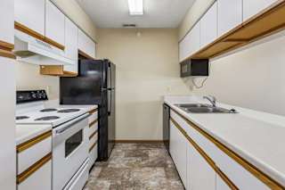 Galley-style apartment kitchen with white cabinets, white oven, black refrigerator, laminate countertops, a double-basin sink, and durable flooring in a functional layout.
