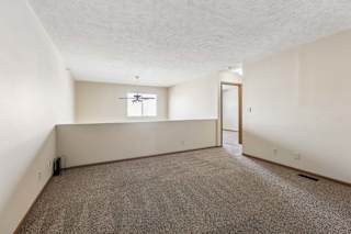 Spacious loft area in an apartment with neutral carpet, a half wall overlooking the lower level, a window for natural light, and an open doorway leading to the hallway.