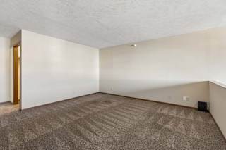 Spacious apartment loft with neutral carpet, a half wall overlooking the living area below, and an open layout with access to the adjoining hallway.