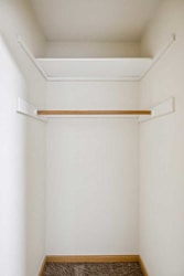 A white wall with a shelf and a brown carpet.