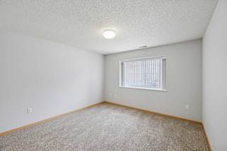 A room with a carpeted floor and a window with blinds.