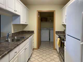 a kitchen with white cabinets, dark counter tops, vinyl flooring, and a white fridge