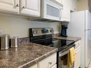 a kitchen with white cabinets, dark grey countertops, a white microwave and glass top stove