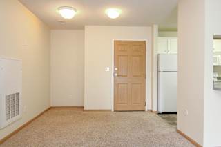 A room with a brown door and a white refrigerator in the background.