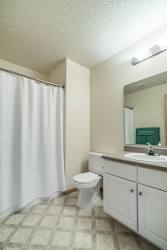 A white toilet sits in a bathroom with a white shower curtain.