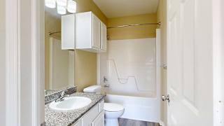 a bathroom with a granite vanity sink, overhead cabinet, and a tub shower