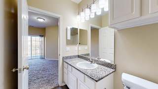 a bathroom attached to the primary bedroom with a vanity sink featuring granite countertops, white cabinets, and large mirrors under modern light fixtures