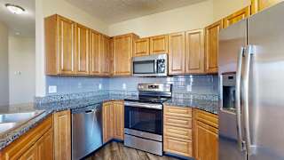 a kitchen with granite countertops, wooden cabinets, a tile backsplash, and stainless steel appliances