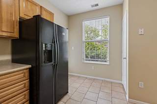 A black refrigerator in a kitchen with wooden cabinets and a window.