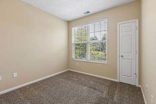 A room with a carpeted floor, a window with blinds, and a white door.