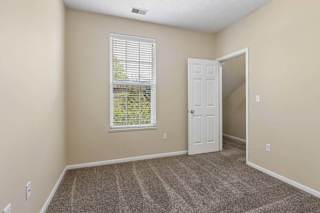 A room with a carpeted floor, a window with blinds, and a door.