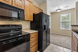 A black refrigerator is in a kitchen with wooden cabinets.