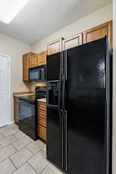 A black refrigerator stands in a kitchen with wooden cabinets and a microwave.